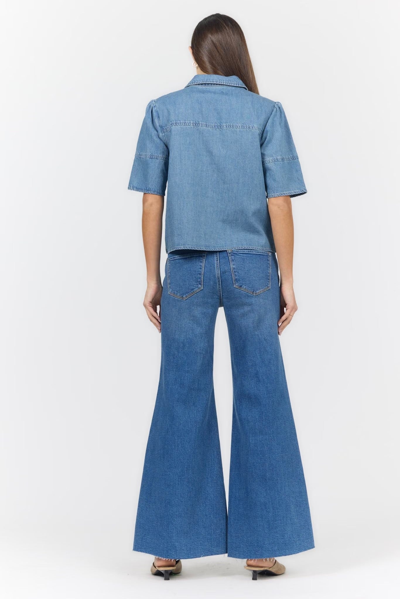 A model viewed from the back wearing a light blue denim short-sleeve button-up shirt and matching wide-leg denim flare pants, set against a plain white studio background.