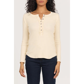 A woman wearing a cream-colored long-sleeve henley top with decorative lace trim and dark navy blue jeans, shown from the neck down against a light gray background.