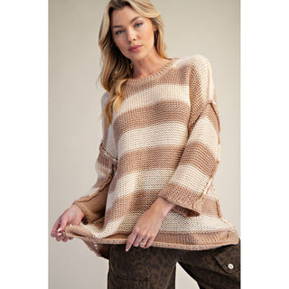 A woman wearing a chunky knit sweater with horizontal stripes in beige and cream, paired with brown leopard-print pants, set against a solid light beige background.