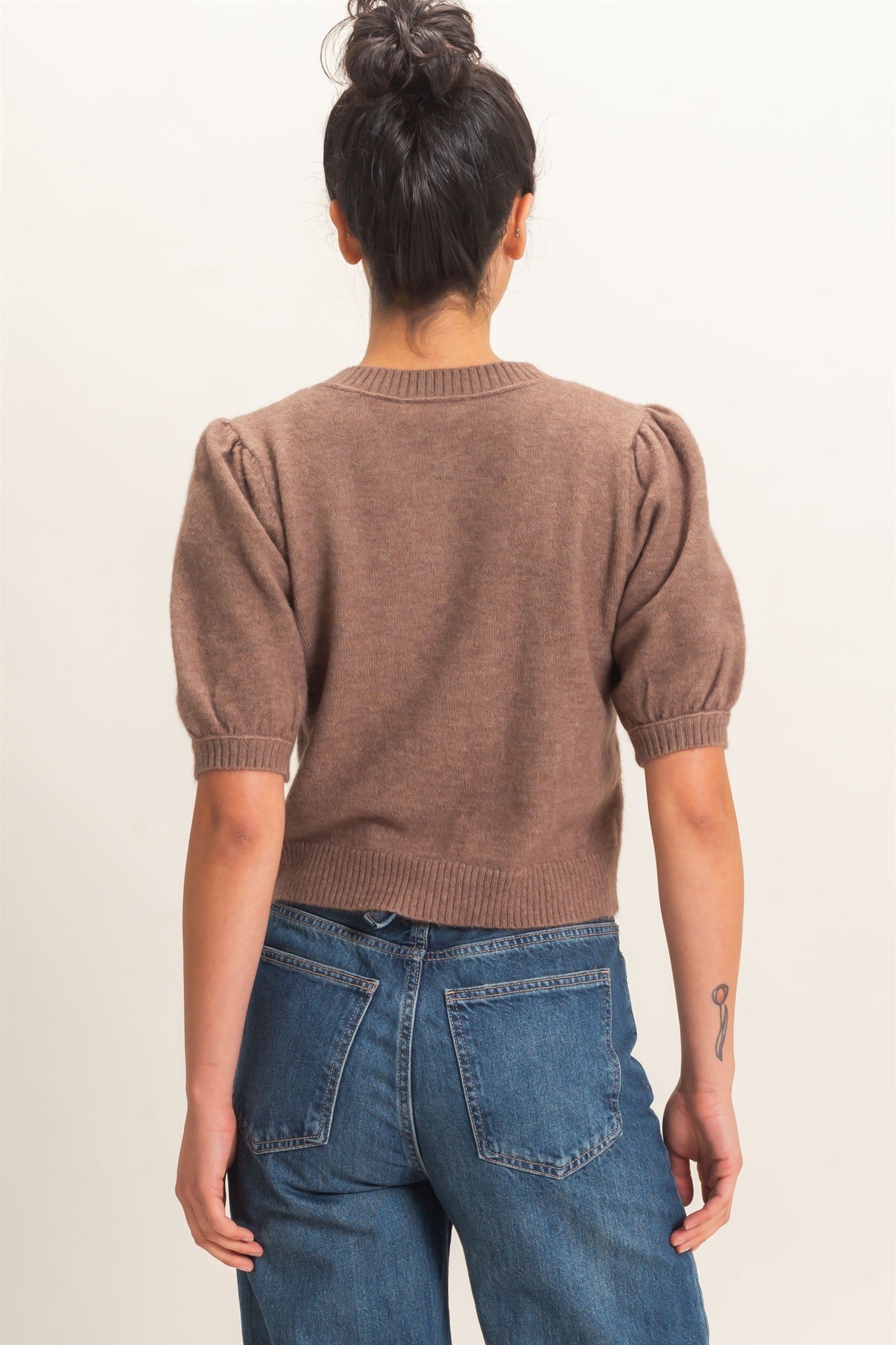 Person wearing a brown sweater and blue jeans against a plain background