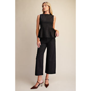 A woman modeling a black sleeveless peplum top and matching black cropped wide-leg pants, paired with brown pointed-toe mule heels, against a plain beige studio background.