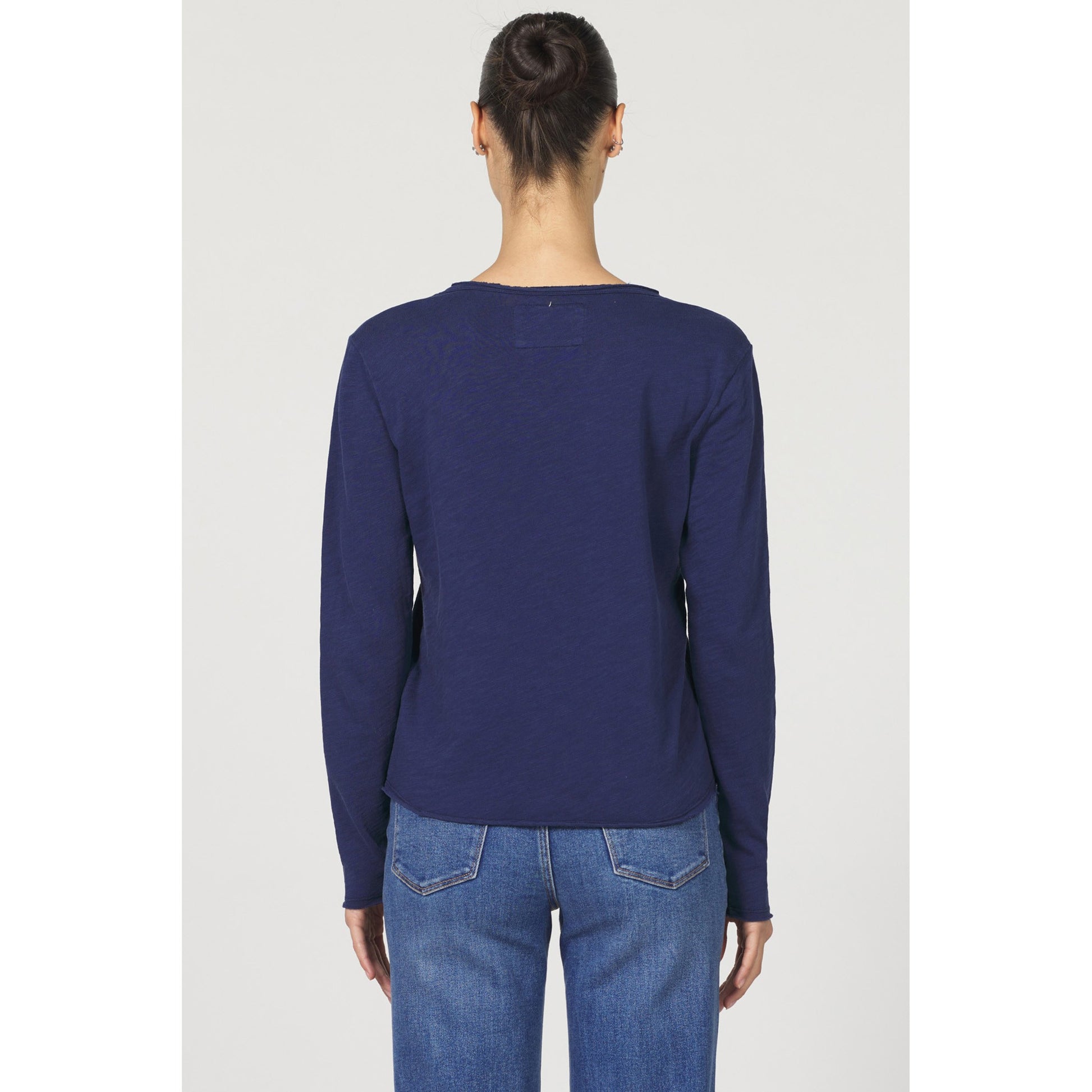 Person wearing a navy long-sleeve shirt and blue jeans on a white background