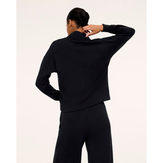A model shown from the back wearing a black cropped long-sleeve athletic jacket and matching black pants against a plain off-white studio background.