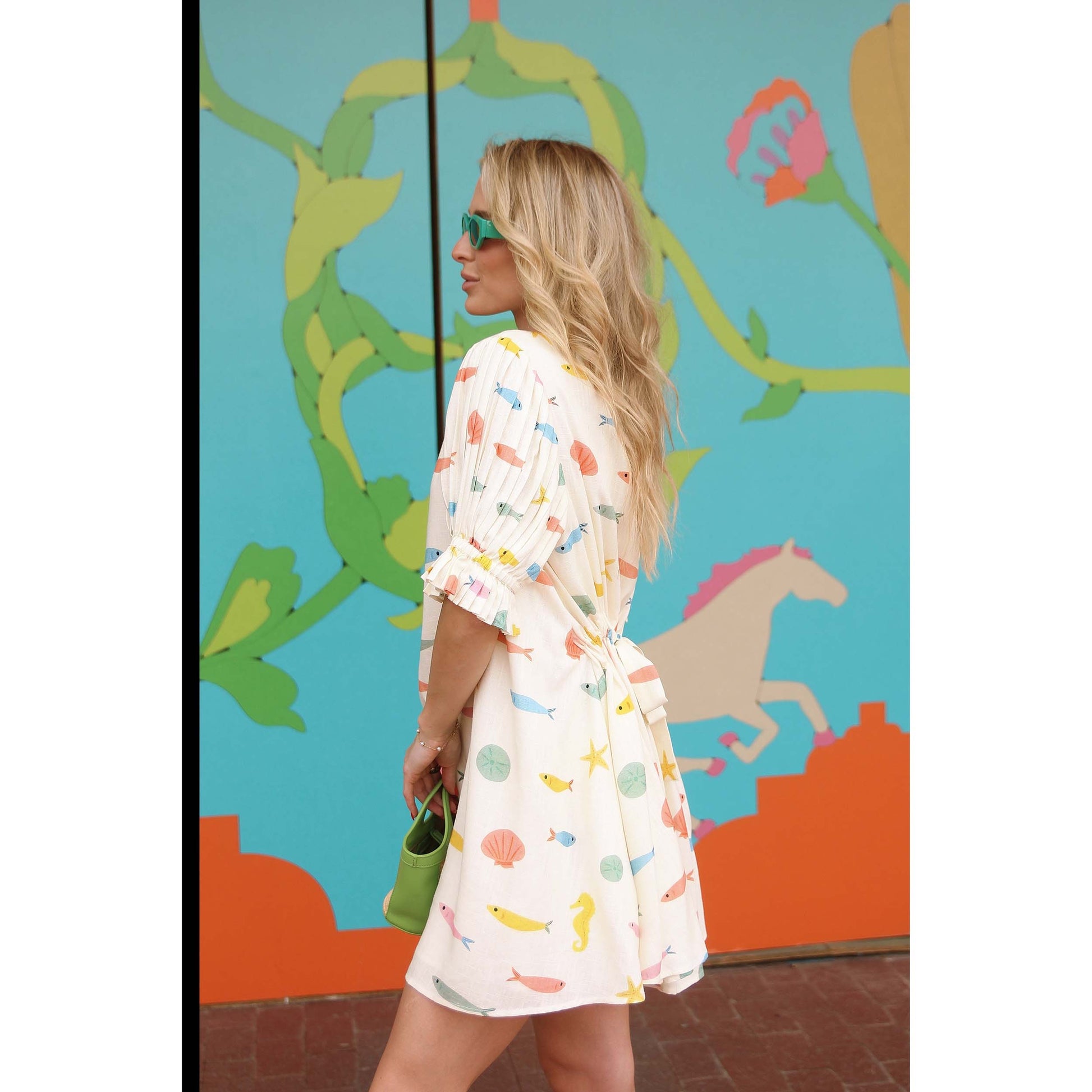Woman in a patterned dress standing in front of a colorful mural.