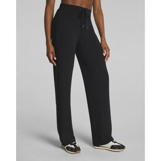 A model wearing black wide-leg sweatpants with a drawstring waistband, paired with black and white sneakers, shown from the waist down against a light gray studio background.