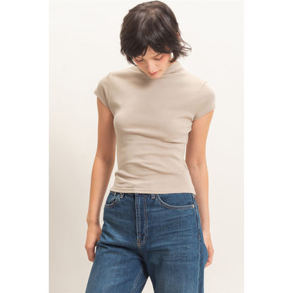 Woman wearing a beige turtleneck top and blue jeans on a white background