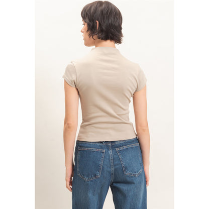 A woman shown from the back wearing a beige short-sleeve mock neck top and blue jeans against a plain off-white background.