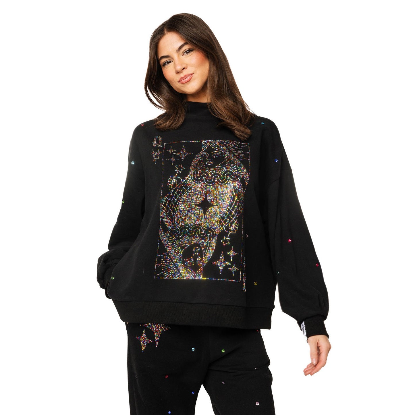 A woman modeling a black crewneck sweatshirt with a large, colorful, psychedelic playing card graphic on the front, styled with matching black pants against a plain white background.