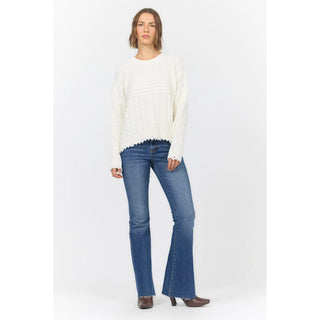 A woman modeling a cream cable-knit sweater and blue flare jeans against a plain white studio background.