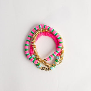 Three stacked stretch bracelets on a light gray background. The top bracelet is made of pink, green, and white striped ribbed bands with a gold-tone clasp.