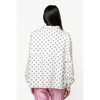 A woman viewed from the back wearing a white long-sleeve top with a black polka dot pattern and pink pants, set against a plain white studio background.