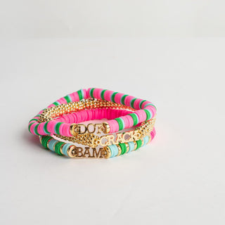 A stack of four beaded bracelets on a light gray background. The bracelets feature pink, green, and light blue beads, with one gold chain bracelet and one gold charm bracelet.