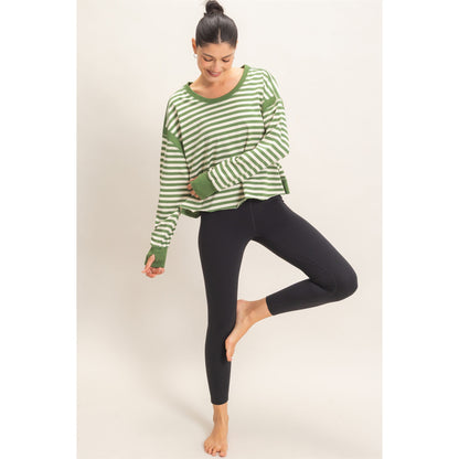 A woman modeling a green and white striped long-sleeve top with black leggings, standing in a yoga tree pose against a plain light beige studio background.