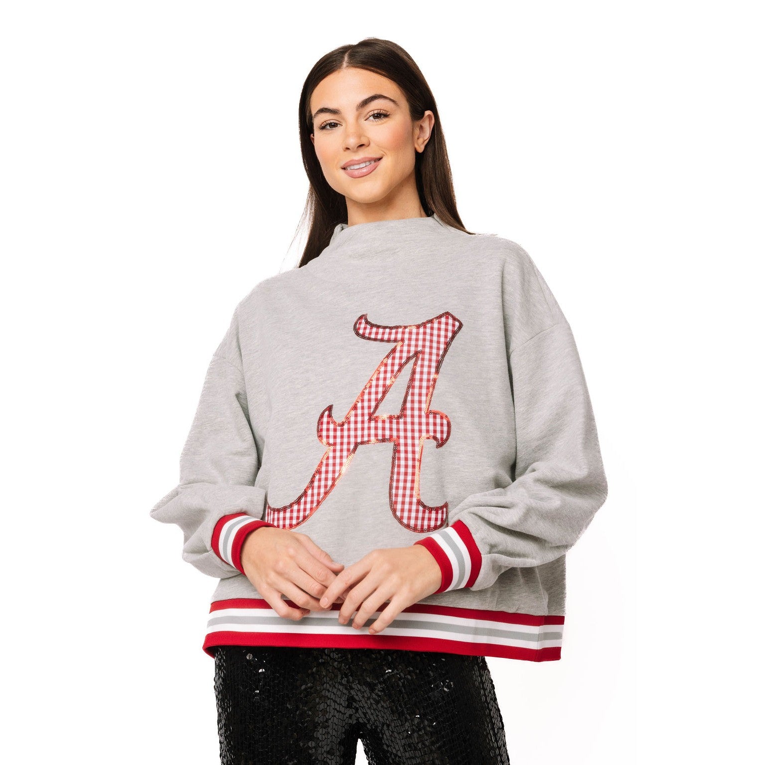 A woman modeling a light gray sweatshirt featuring a large red and white gingham checkered Alabama 'A' logo on the front, with red and white striped ribbed cuffs and hem, set against a plain white background.