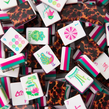 A pile of rectangular playing cards with a mahjong-inspired design, featuring leopard print backs, colored stripes, and illustrated tiles on a white background.