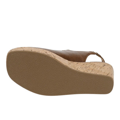 A close-up of a wedge sandal's sole, showing a textured tan rubber outsole and a cork-look midsole with a brown leather upper strap, on a white background.